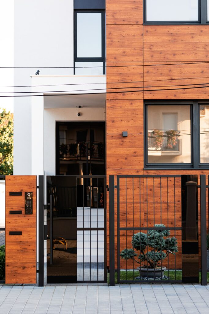 Entrada moderna a vivienda con fachada de paneles efecto madera, puerta metálica negra y diseño minimalista en entorno urbano.